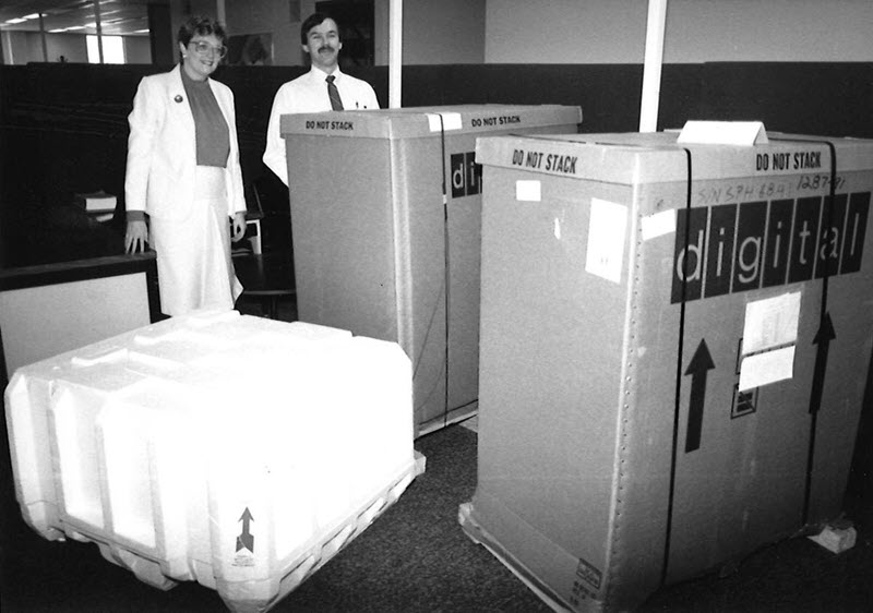 Photo en noir et blanc d'une femme et d'un homme debout derrière deux boîtes qui sont presque aussi grandes qu'eux, avec le mot « digital » écrit sur le devant.