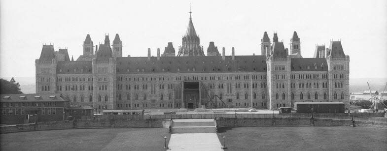 Photo en noir et blanc d'un long bâtiment symétrique de quatre étages avec fenêtres en arc et une entrée principale au centre