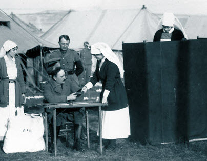 Une photographie en noir et blanc de 1917: une infirmière militaire canadienne remet un document à un homme assis à une table de bureau