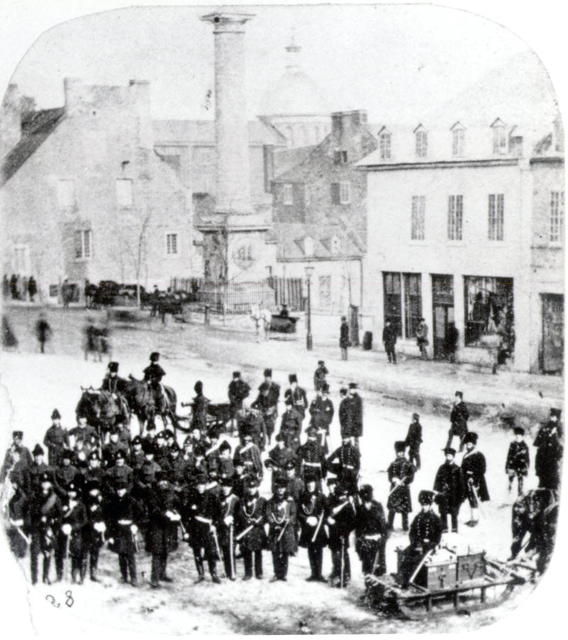 Black and white photo of a crowd of uniformed officers gathering on a city street in front of a white building.