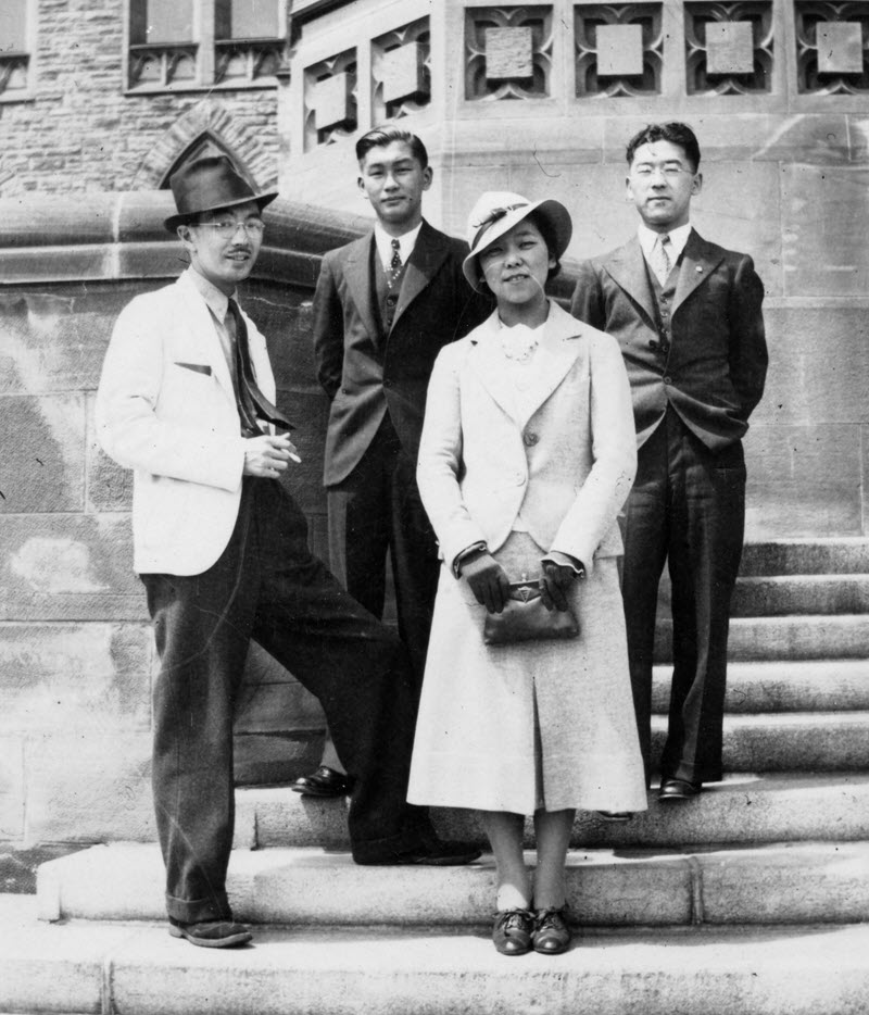 Black-and-white photo of a group of three Japanese men and one Japanese woman standing on the steps of Parliament.