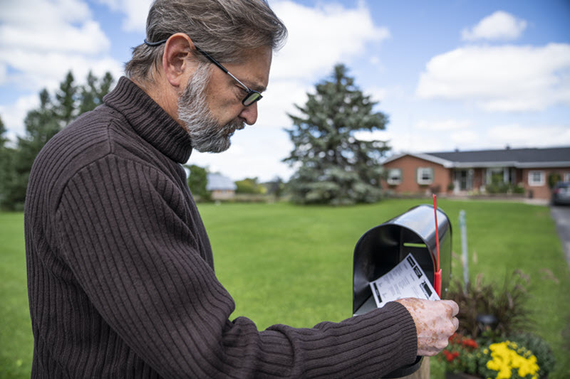 Colour photo of a man receiving a voter information card in his standing mailbox.