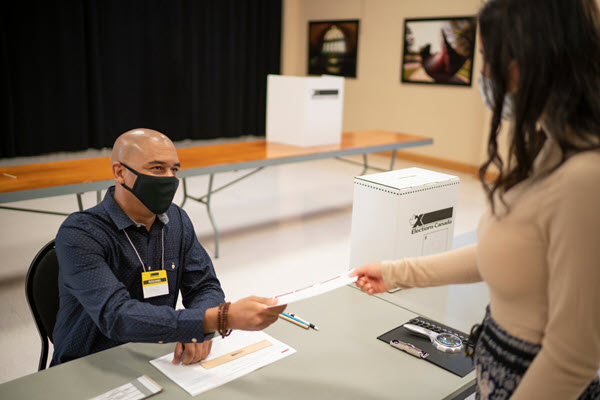 Préposé au scrutin seul à la table de service et portant un masque